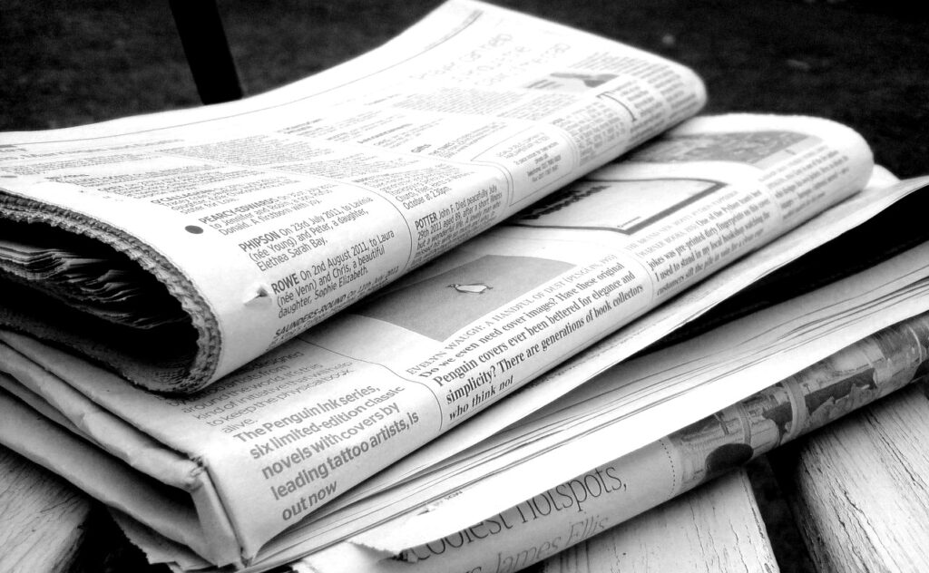 Black and white image of three newspapers stacked on top of each other on a wooden surface. 